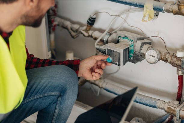 Young construction worker checking heating installations in a new building he is working on. Handsome young engineer in safety gear setting installations on a construction site. Heating engineer working with a digital tablet.