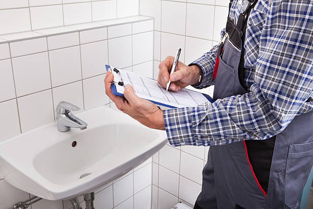 Close-up Of Plumber Standing In Front Of Washbasin Writing On Clipboard